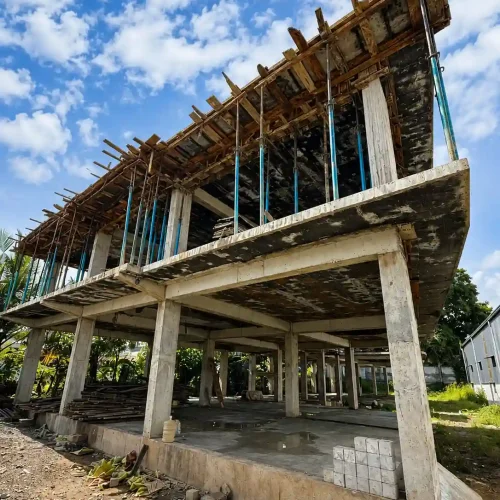 Unfinished concrete building under construction with exposed columns, slabs, scaffolding, and wooden formwork, highlighting structural engineering and construction work by a structural engineering company in kochi.